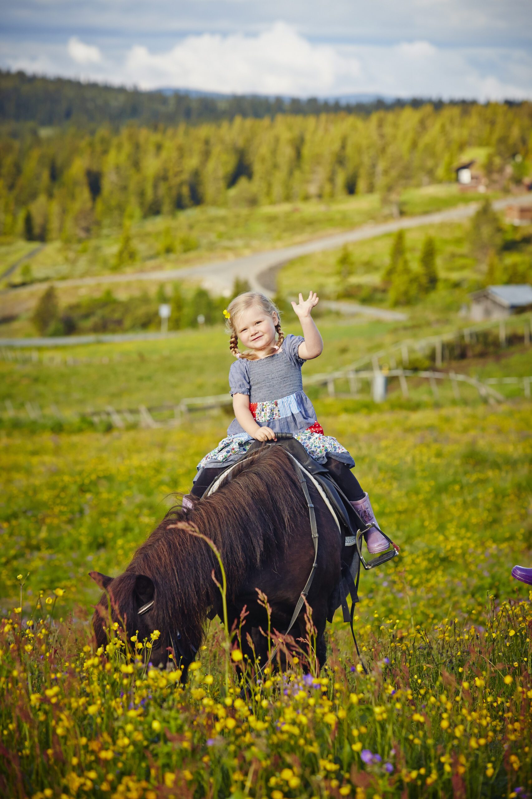 Liten jente sitter på ponny og vinker